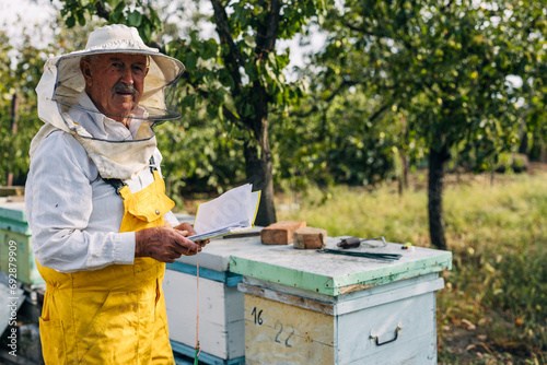 Senior apiarist standing outdoor in a beekeepers suit and looking at the camera