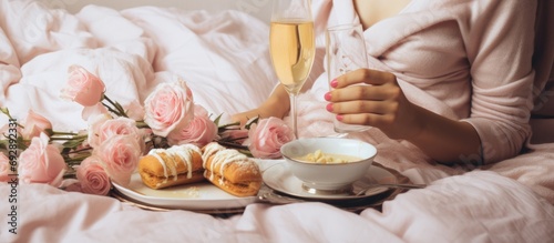 Woman with flowers and surprise gift, enjoying romantic breakfast in bed on Valentine's Day with champagne and croissants. Happy Mother's Day.