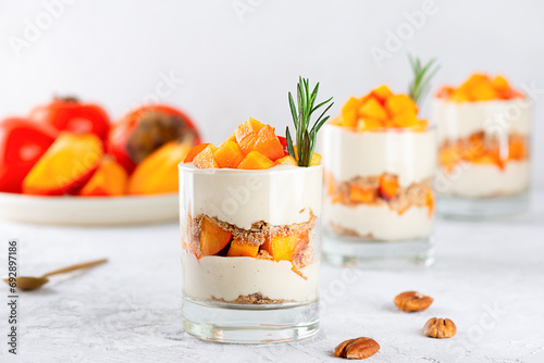 Parfait in a glasses with persimmon, pecan, whipped cream and rosemary on a table. Healthy food, vegan, sugar, gluten and lactose free.
