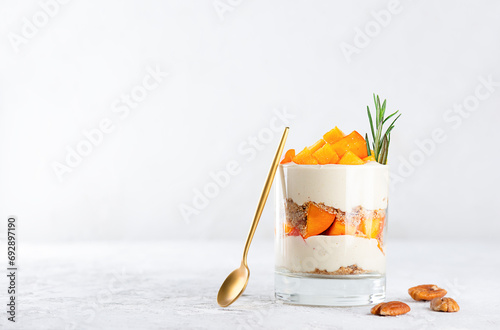 Dessert in a glass with persimmon, rosemary, pecan, whipped cream and spoon. Healthy food, vegan, sugar, gluten and lactose free.