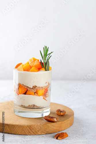 Dessert in a glass with persimmon, rosemary, pecan, whipped cream and biscuit on a wooden board. Healthy food, vegan, sugar, gluten and lactose free.