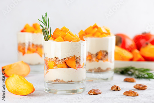 Dessert in a glasses with persimmon, pecan, whipped coconut cream, biscuit and rosemary. Healthy food, vegan, sugar, gluten and lactose free.