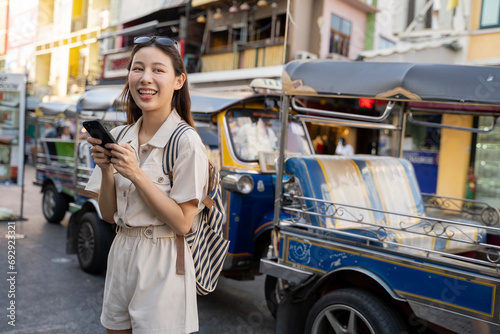 Happy young travel Asian woman using a mobile phone in a street market at dusk in Bangkok, Thailand, Travel vacation city concept