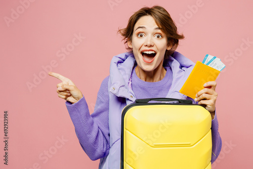 Traveler woman wear purple casual clothes hold passport ticket bag point aside isolated on plain pink background. Tourist travel abroad in free spare time rest getaway Air flight trip journey concept