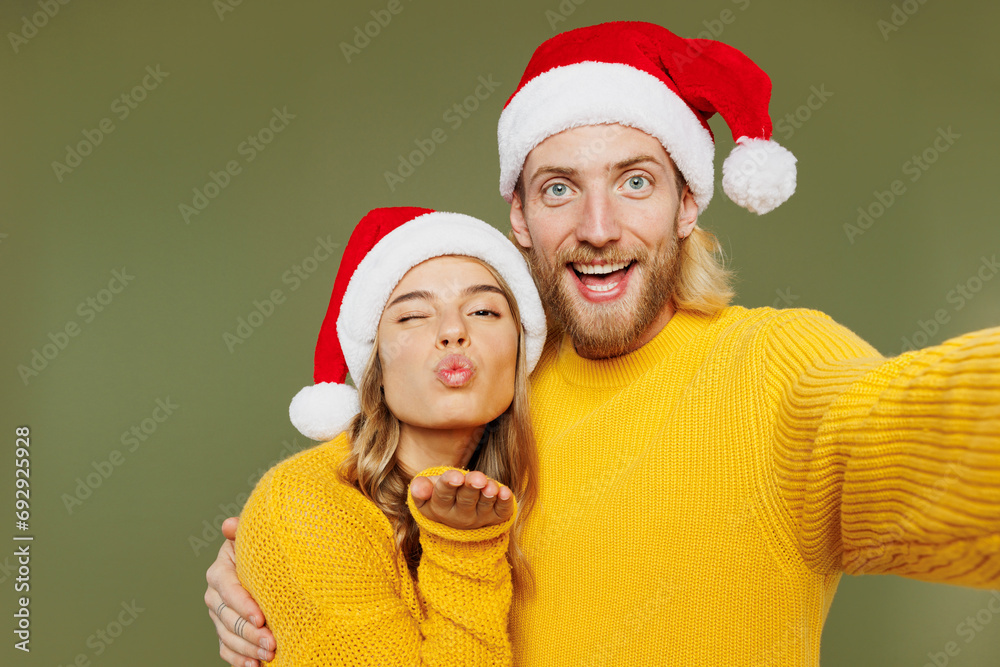 Close up young couple two friends man woman wear sweater Santa hat posing do selfie shot on mobile cell phone blow air kiss isolated on plain green background Happy New Year Christmas holiday concept Close up young couple two friends man woman wear sweater Santa hat posing do selfie shot on mobile cell phone blow air kiss isolated on plain green background Happy New Year Christmas holiday concept