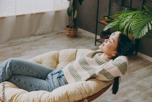 Top view sideways young woman wears casual clothes hold hands behind neck close eyes sits on armchair stays at home flat rest relax spend free spare time in living room indoor. People lounge concept. #692927744
