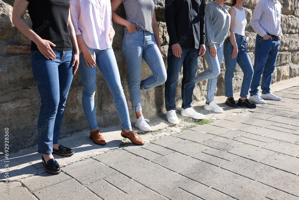 Group of people in stylish jeans near stone wall outdoors on sunny day, closeup