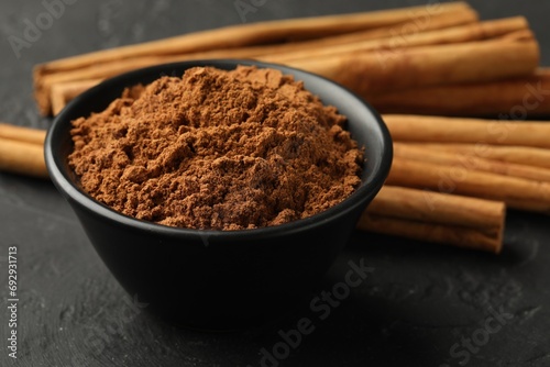 Aromatic cinnamon powder and sticks on black table, closeup