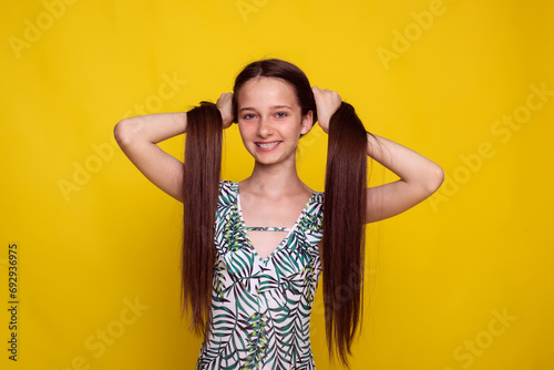 proper long hair care in summer, teen girl make ponytails on yellow studio background. no split ends hair photo