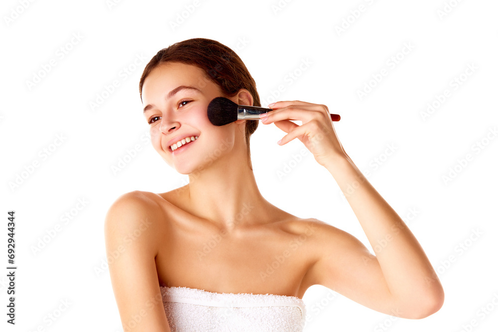 Natural makeup look. Young smiling beautiful girl with smooth, well-kept, spotless skin applying blush on cheeks over white background. Concept of natural beauty, skin care, cosmetology and cosmetics