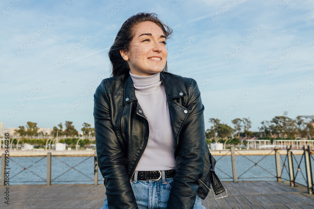 Smiling woman in leather jacket sitting on embankment Smiling woman in leather jacket sitting on embankment
