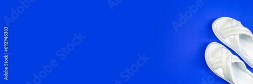 White leather women's slippers stand on a blue background. Slippers are located at an angle. View from above. A part of the shoe is visible. Horizontal image. Banner for insertion into site.