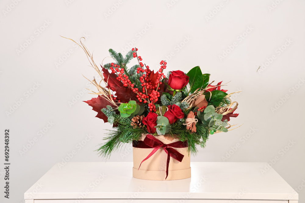 Sombrerera de flores navideña rojas sobre mesa blanca y fondo neutro
