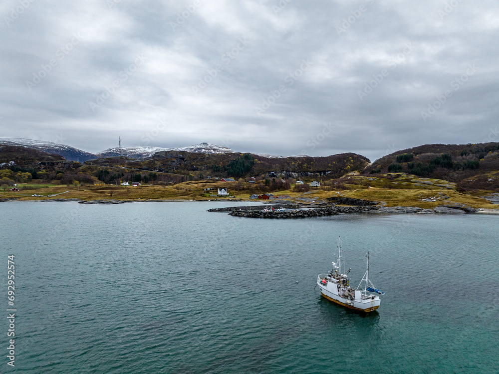 aerial view from drone of a small fisherman boat next to a rocky shore of norwegian sea with cyan blue water