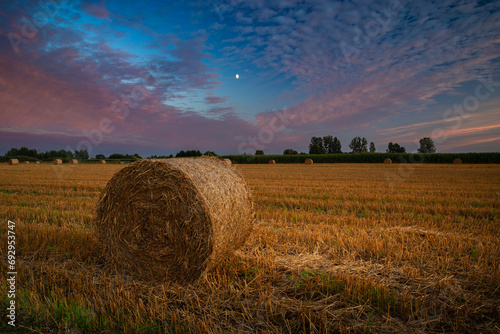 A large bale of hay on a stubble field and a beautiful sunset on an August evening