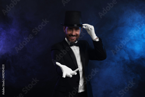 Happy magician wearing top hat in smoke on dark background