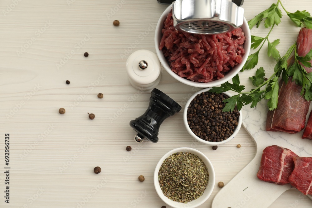 Meat grinder, beef, parsley and spices on white wooden table, flat lay. Space for text Meat grinder, beef, parsley and spices on white wooden table, flat lay. Space for text