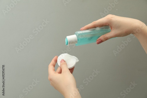 Woman pouring makeup remover onto cotton pads on light grey background, closeup