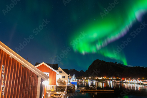 beautiful northern lights over S  rv  gen village with red fisherman cabins on shore of lofoten islands