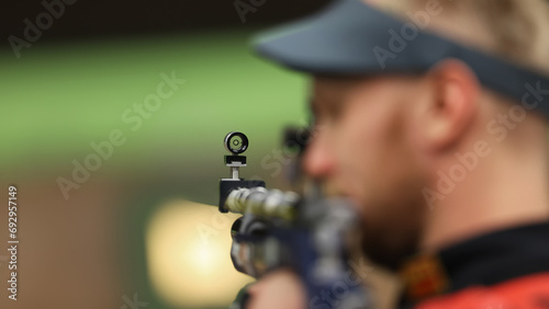 A male athlete shoots with an air rifle. Selective focus on the front sight of the rifle.