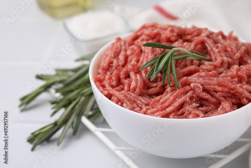 Fresh raw ground meat and rosemary in bowl on light table, closeup. Space for text
