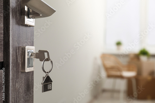 Mortgage and real estate. Open door with key and house shaped keychain against blurred background, space for text photo