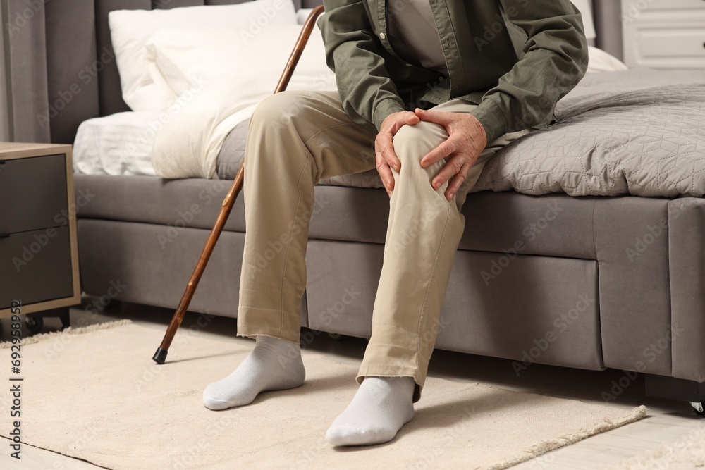Senior man with walking cane suffering from knee pain on bed at home, closeup. Rheumatism symptom - obrazy, fototapety, plakaty 