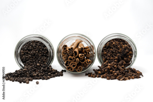 spill out spices from glass jar, black peppercorn, cinnamon and cloves, isolated on white background, concept of spice catalog, eye level shot