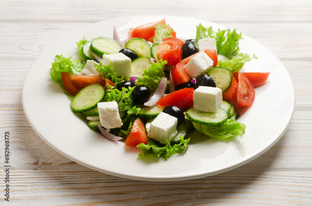 Classic Greek salad with cucumbers, tomatoes, red onion, feta cheese, lettuce and black olives on a white wooden table. The concept of traditional dishes. Healthy food. Simple ingredients. Classic Greek salad with cucumbers, tomatoes, red onion, feta cheese, lettuce and black olives on a white wooden table. The concept of traditional dishes. Healthy food. Simple ingredients.