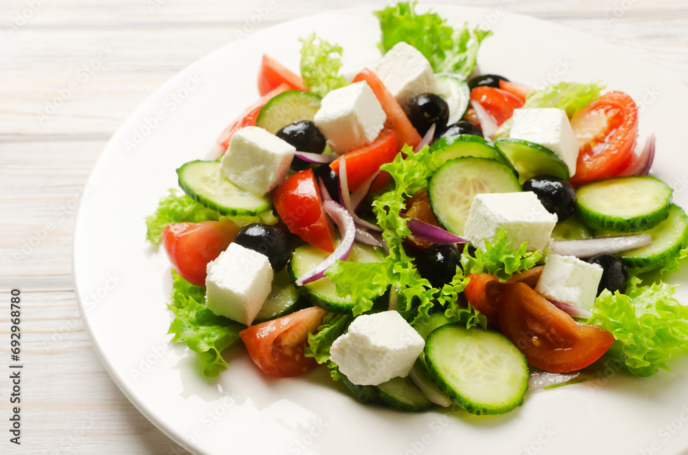 Classic Greek salad with cucumbers, tomatoes, red onion, feta cheese, lettuce and black olives on a white wooden table. The concept of traditional dishes. Healthy food. Simple ingredients. Classic Greek salad with cucumbers, tomatoes, red onion, feta cheese, lettuce and black olives on a white wooden table. The concept of traditional dishes. Healthy food. Simple ingredients.