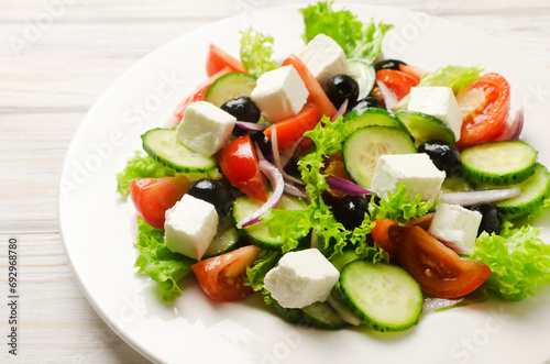 Classic Greek salad with cucumbers, tomatoes, red onion, feta cheese, lettuce and black olives on a white wooden table. The concept of traditional dishes. Healthy food. Simple ingredients.