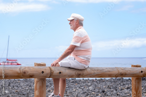 Portrait of relaxed caucasian bearded man with hat sitting at the beach looking at the horizon while enjoying vacation or retirement. Horizon over the water, copy space photo