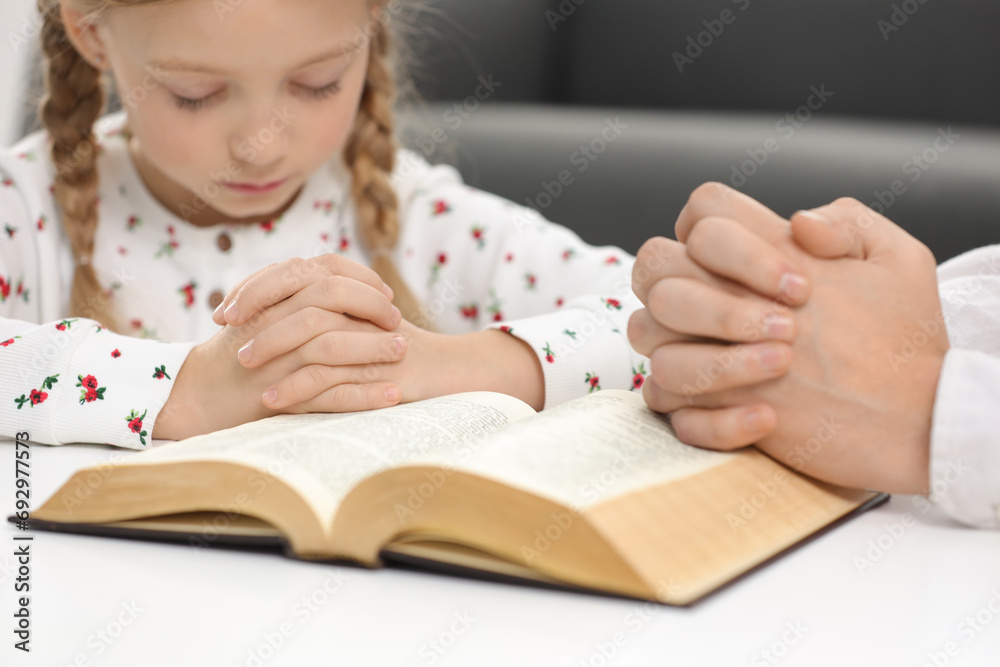 Girl and her godparent praying over Bible together at table indoors, selective focus Girl and her godparent praying over Bible together at table indoors, selective focus