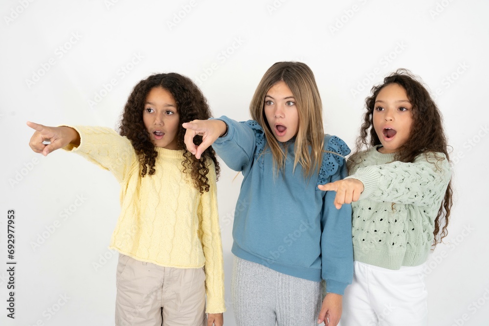 multi racial group of girl friends Pointing with finger surprised ahead, open mouth amazed expression, something on the front.