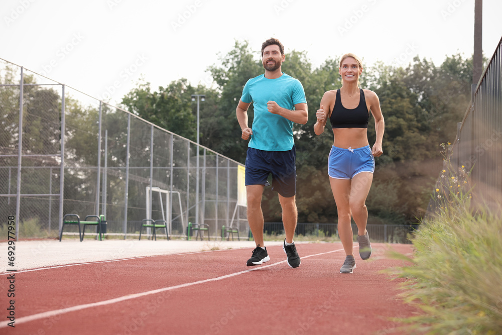 Healthy lifestyle. Happy sporty couple running at stadium, space for text