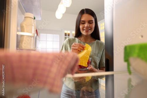 Happy woman taking away beeswax food wrap, view from refrigerator photo