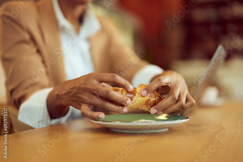 Close-up of a female, splitting a croissant, eating breakfast in the cafe.