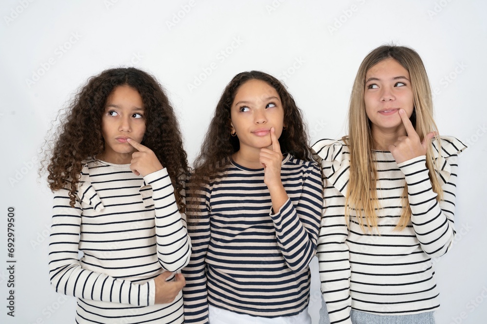 Lovely dreamy multi racial group of girl friends keeps finger near lips looks aside copy space. Lovely dreamy multi racial group of girl friends keeps finger near lips looks aside copy space.