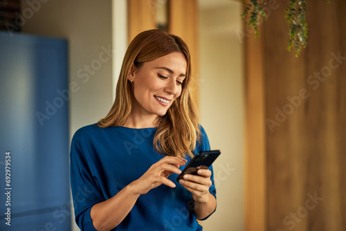 Side view of a smiling woman, chatting with someone over the mobile phone while standing in the kitchen.