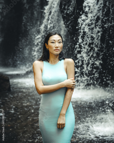 Portrait of Asian woman posing near the waterfall. Nature and environment concept. Travel lifestyle. Beautiful woman wearing light blue dress. Copy space. Yeh Bulan waterfall in Bali