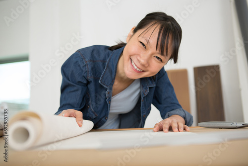 young woman doing repairs in apartment - wallpapering on wall