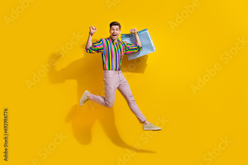 Full size body photo of young gay man jumping with paper packages shopping bags new collection gucci isolated on yellow color background