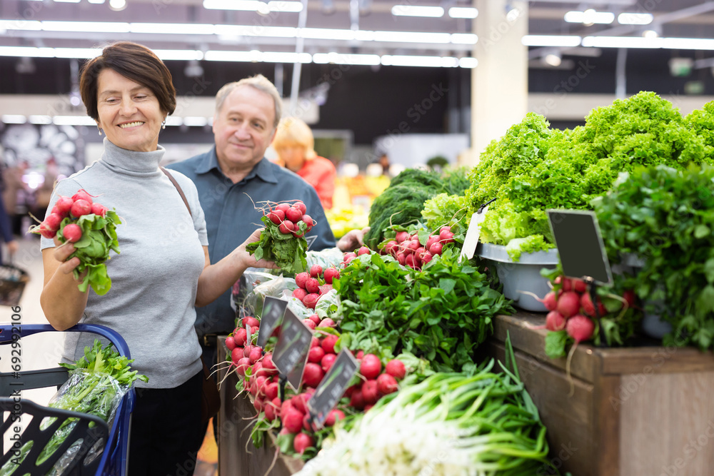 Smiling happy couple is choosing bell peppers and other vegetables in supermarket