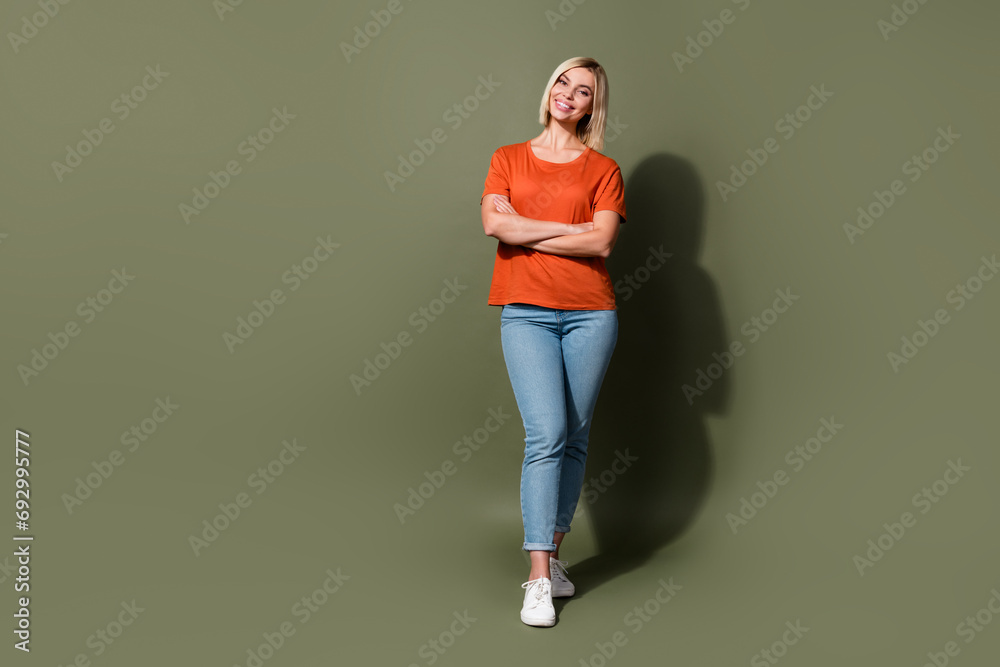 Full body size view photo of blonde bob hair girlfriend in orange t shirt with skinny jeans folded hands isolated on khaki color background Full body size view photo of blonde bob hair girlfriend in orange t shirt with skinny jeans folded hands isolated on khaki color background