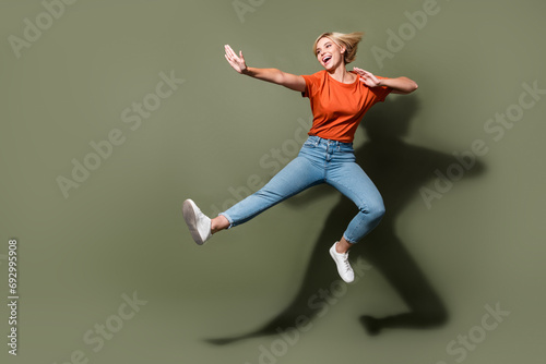 Full length photo of impressed young girl dressed orange t shirt jumping high combat practicing fighting isolated on khaki color background