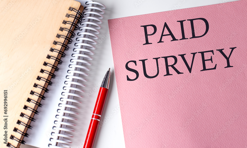 PAID SURVEY word on the pink paper with office tools on white background PAID SURVEY word on the pink paper with office tools on white background