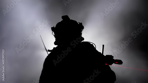 Silhouette military soldier, warrior aims by weapon assault rifle carbine with tactical red laser sight. Shadow mercenary in army camouflage. War concept. Fog smoke in background. Uniform and helmet photo
