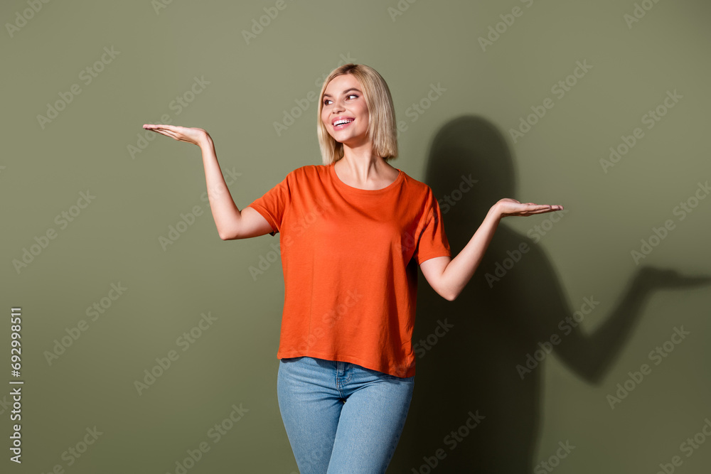 Photo portrait of attractive young woman hold compare empty space wear trendy orange clothes isolated on khaki color background Photo portrait of attractive young woman hold compare empty space wear trendy orange clothes isolated on khaki color background