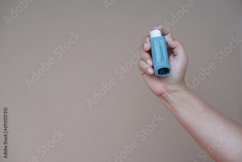 Close up woman hand hold asthma inhaler, brown background. Concept, health care. Pharmaceutical products for treatment symptoms of asthma or COPD. Use under prescription. Health care device at home. 