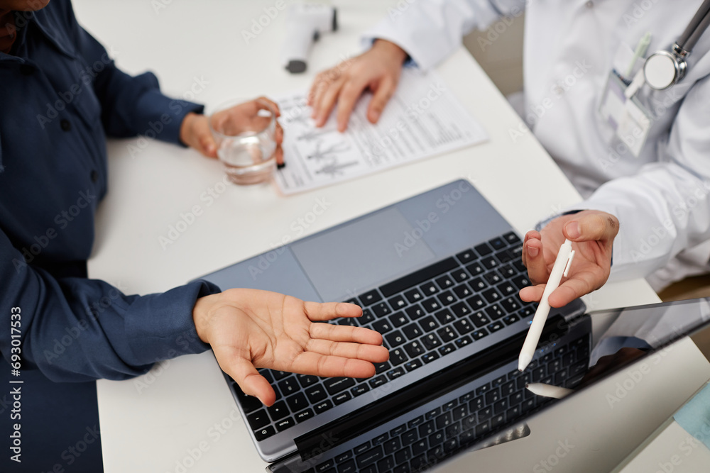 Top view of unrecognizable physician and patient using wireless laptop while discussing diagnosis and treatment at clinic Top view of unrecognizable physician and patient using wireless laptop while discussing diagnosis and treatment at clinic